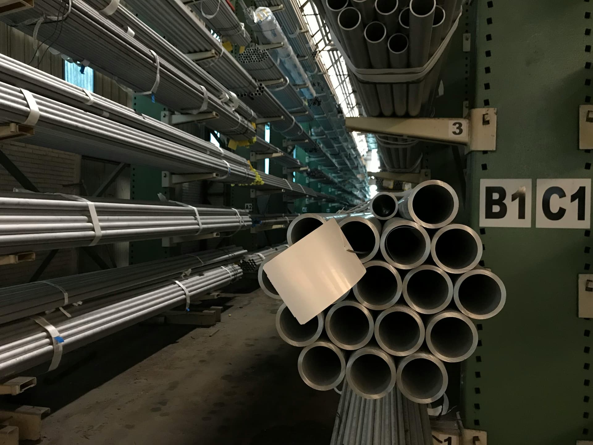 Un conjunto de tubos galvanizados apilados, algunos de ellos con marcas de uso y suciedad. Los tubos tienen un acabado metálico brillante y se disponen de manera ordenada, mostrando sus extremos redondeados.