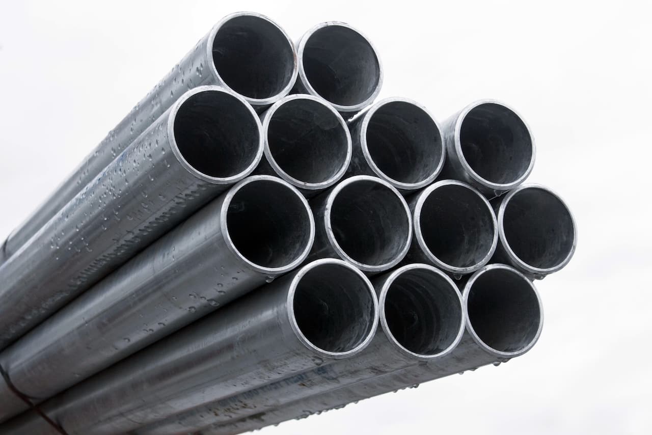 Un grupo de tubos galvanizados apilados en forma de pirámide, con superficie brillante y gotas de agua en algunas partes, bajo un cielo nublado.