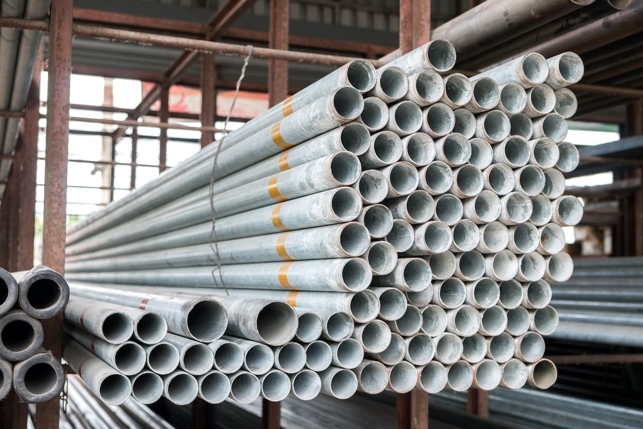 Un conjunto de tubos galvanizados apilados, algunos de ellos con marcas de uso y suciedad. Los tubos tienen un acabado metálico brillante y se disponen de manera ordenada, mostrando sus extremos redondeados.